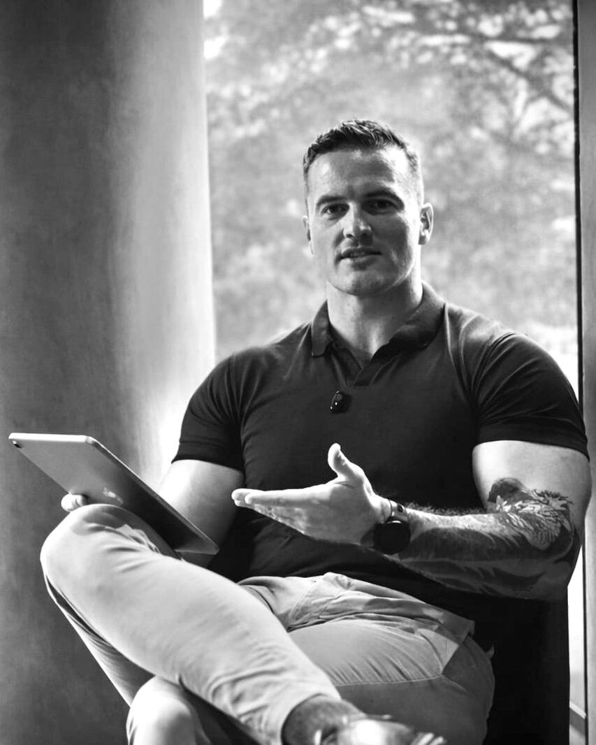 James Richman seated by a window, holding a tablet in one hand and explaining a point with the other.