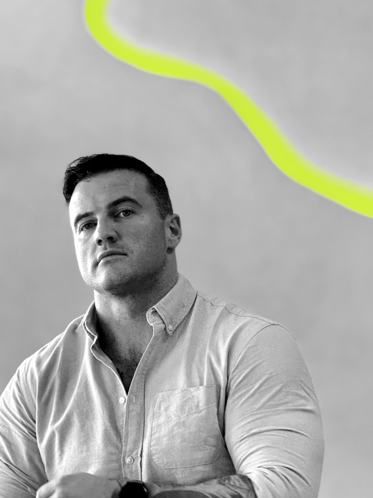 James Richman in a light shirt, looking at the camera, under an arc of light on a pale wall.